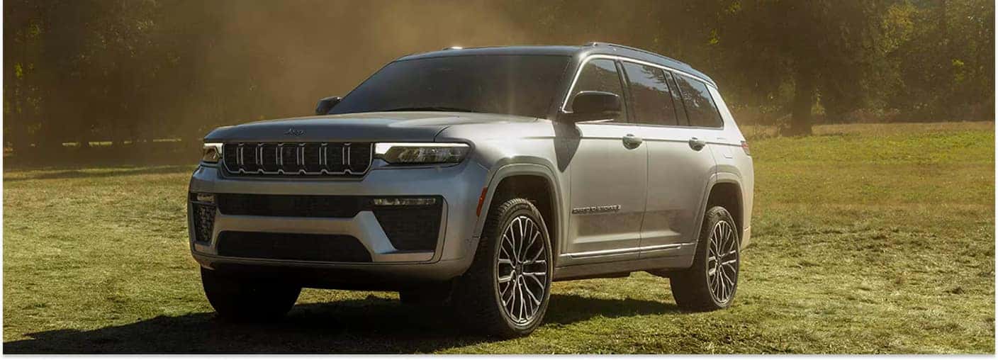 Silver 2026 Jeep Grand Cherokee parked in an open grassy field.