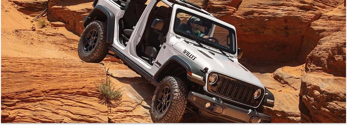 White 2026 Jeep Wrangler Willys driving without doors over red rock terrain.