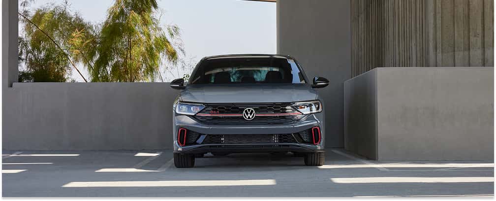 Gray 2026 Volkswagen Jetta GLI sedan parked in a modern concrete structure, front view.