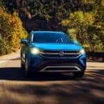 A blue 2022 Volkswagen Taos is shown driving on a mountain road after leaving an Akron VW dealership.