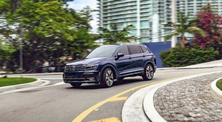 A blue 2021 used Volkswagen Tiguan is shown rounding a corner on a city street.