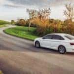 A white 2021 Volkswagen Jetta SEL is shown driving on a country road after leaving a used Volkswagen dealership.