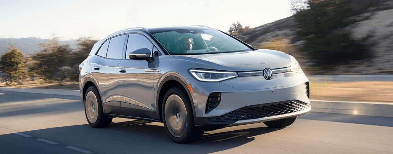 A grey 2023 Volkswagen ID.4 Electric Vehicle is shown from a front angle driving on an open highway.