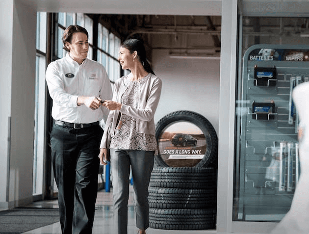 A dealership manager handing over a set of car keys to a lady.
