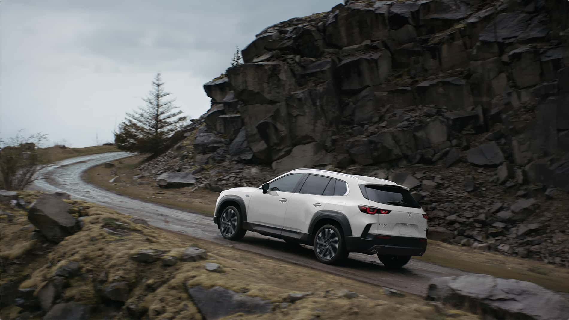 A white Mazda CX-50 driving up a hill