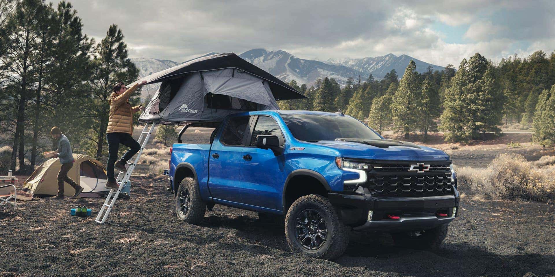 people putting up a pop up camper in the back of a blue chevy truck in the wilderness