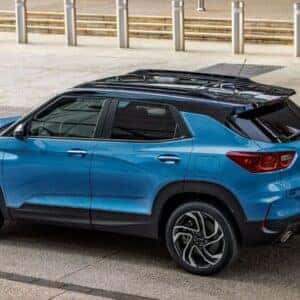 Overhead side view of the 2025 Chevrolet Trailblazer in a vibrant blue finish, highlighting its sleek roof design, sporty alloy wheels, and modern styling, parked in a contemporary urban setting.