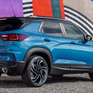 Rear and side view of the 2025 Chevrolet Trailblazer in a vibrant blue finish, showcasing its sleek design, dual exhaust, and bold alloy wheels, set against a colorful urban mural.