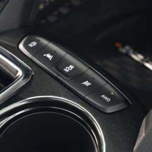 Close-up of the drive mode selector in the 2025 Chevrolet Trailblazer, featuring controls for traction, off-road, and AWD modes, positioned next to the gear shifter and cup holder.