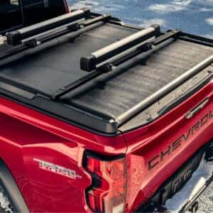 The bed of a red Chevrolet Colorado Trail Boss featuring a snow-covered tonneau cover and rail system.