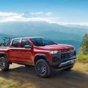 A red Chevrolet Colorado with a bike in the bed driving on a scenic mountain road.