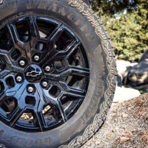 Close-up of the rugged black alloy wheel and all-terrain tire of a Chevrolet Colorado Trail Boss on rocky terrain.