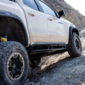 A white Chevrolet Colorado navigating rocky terrain with off-road tires in a rugged landscape.