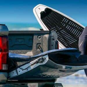 A Chevrolet Colorado Z71 by the beach, with a man carrying a surfboard near the tailgate.
