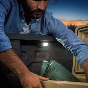 A man reaching into the bed of a Chevrolet Colorado truck with built-in LED lighting at dusk.