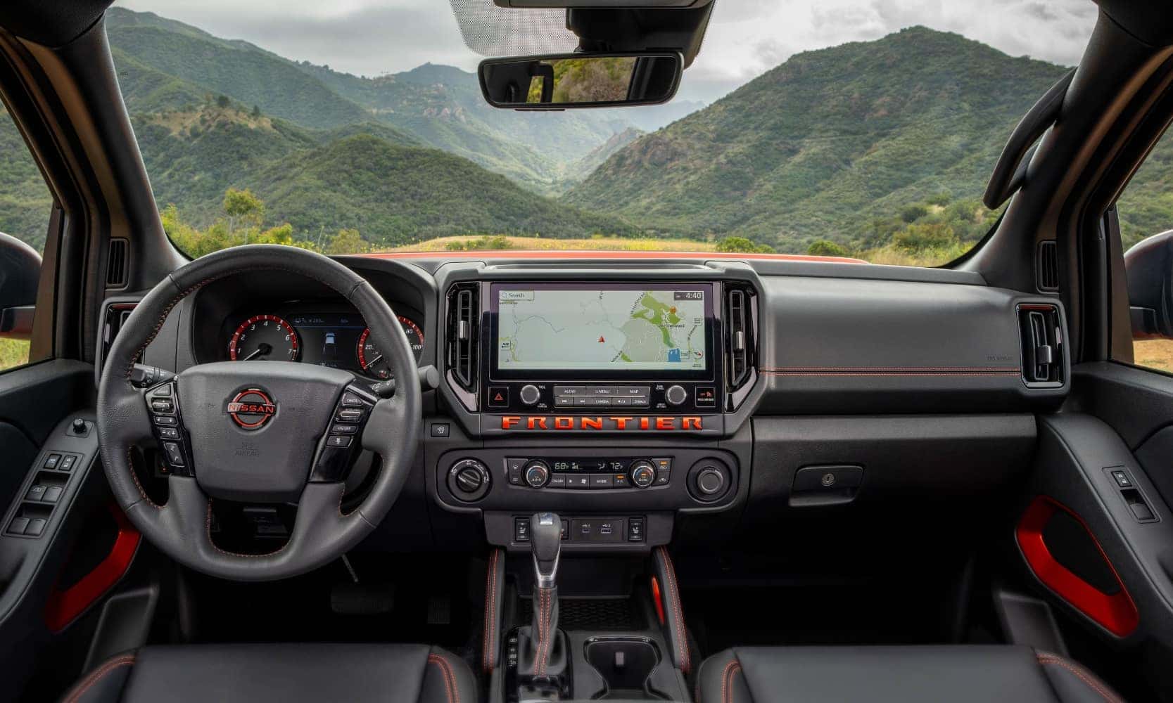 Interior image of a 2025 Nissan Frontier front seating area with orange stitch accents, dashboard, and mountain views from the windshield