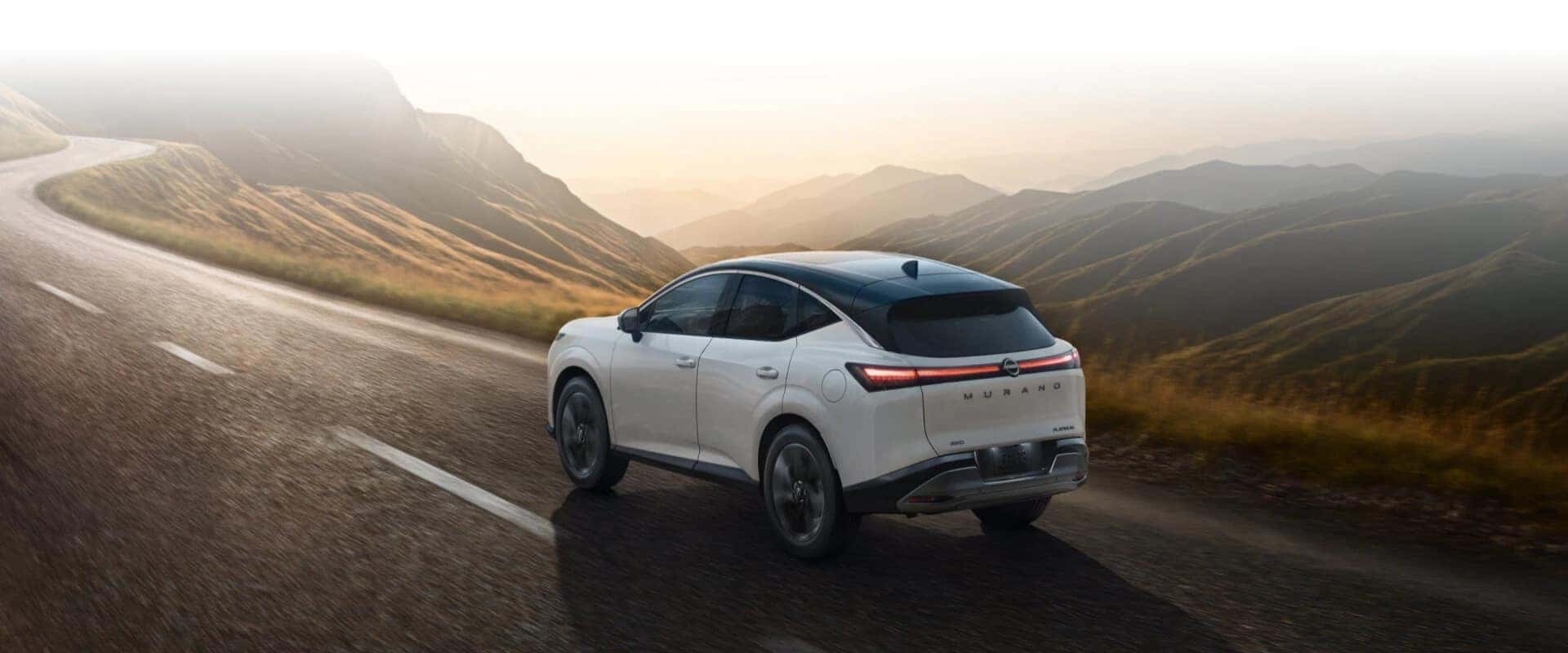 Hero exterior rear image of a white 2025 Nissan Murano driving down a mountainous freeway