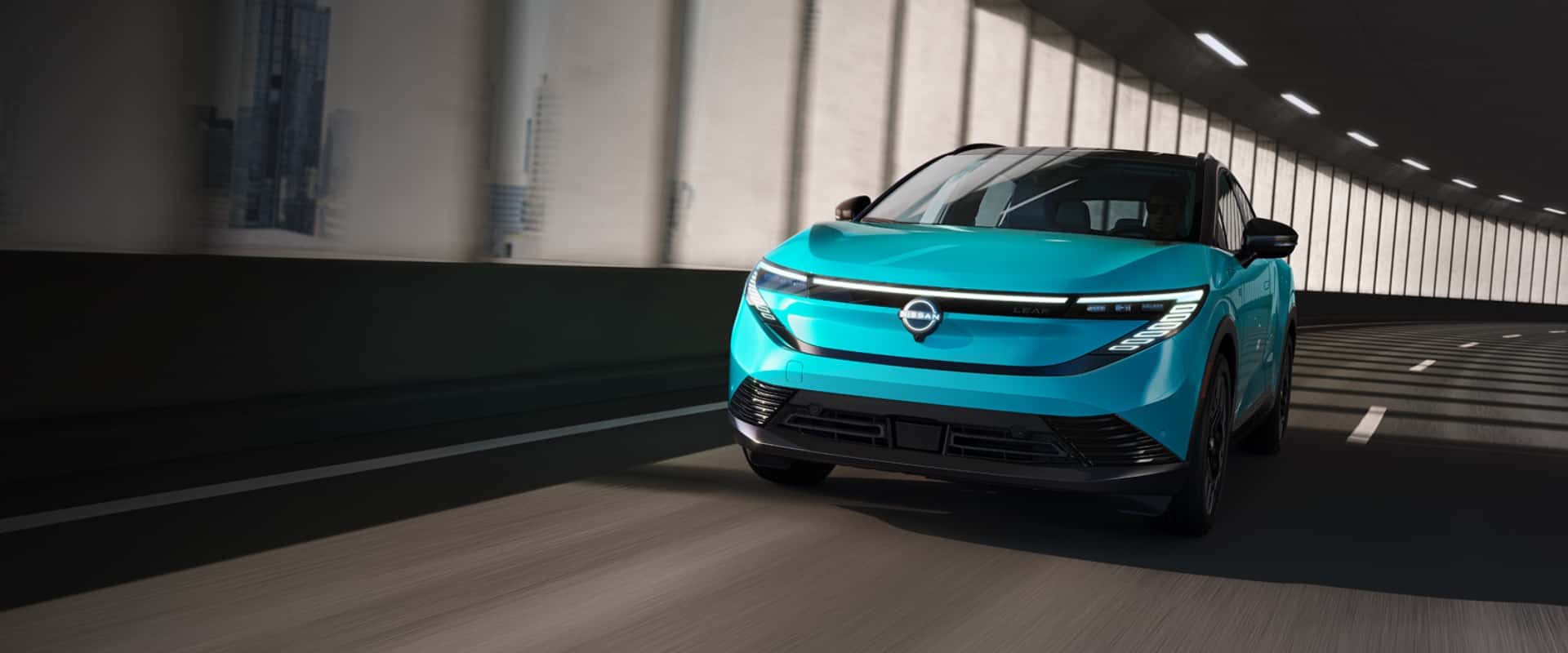 Exterior front hero image of an aqua blue 2026 Nissan LEAF Platinum+ driving down an enclosed freeway