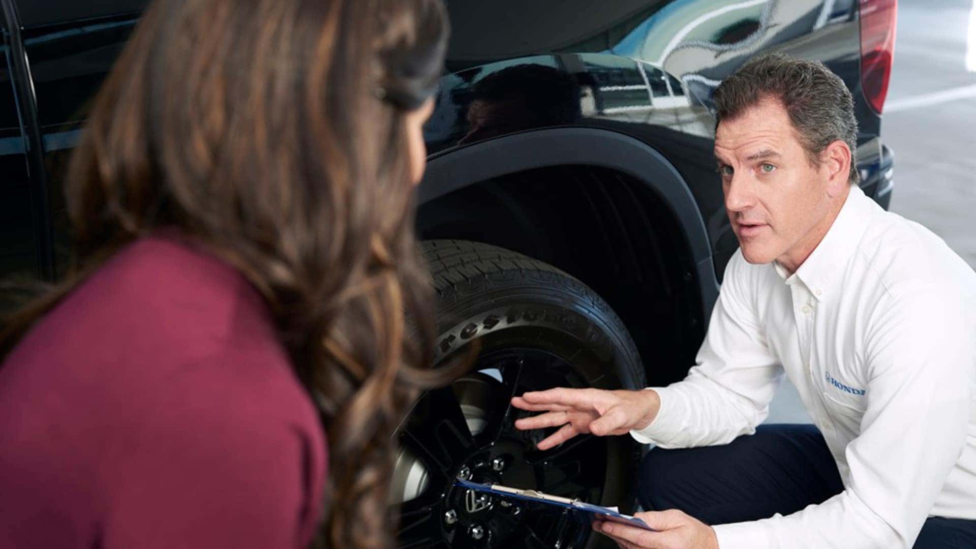 honda dealership worker talking to woman next to tire