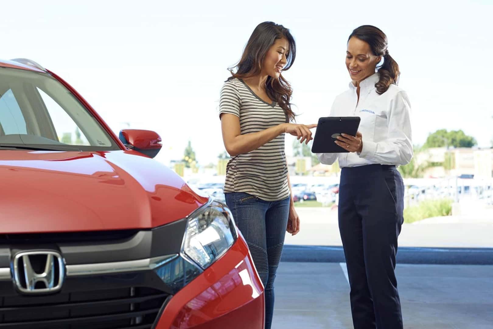 sales person helping woman look at cars standing next to red honda vehicle