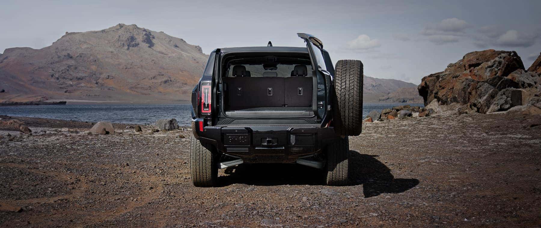GMC SUV with rear door open outside near water and rocky terrain