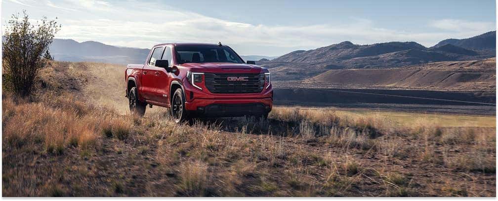 Front three-quarter view of a red 2026 GMC Sierra 1500 driving on a dirt trail.