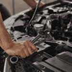 Mechanic holding wrenches while inspecting vehicle engine