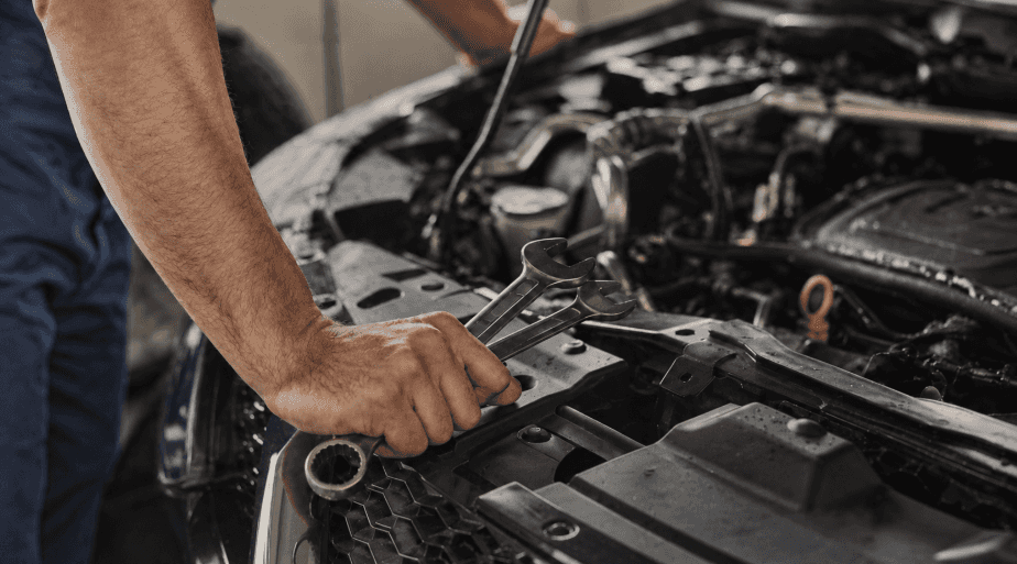 Mechanic holding wrenches while inspecting vehicle engine