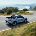 A blue Hyundai Santa Cruz driving down the road heading towards the beach.