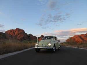 A yellow 1963 VW Bug parked in front of the setting sun.