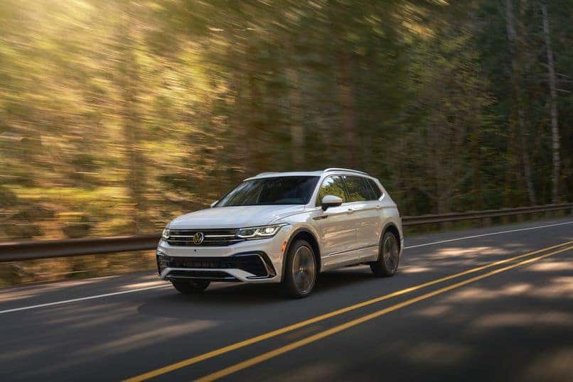 A white 2022 Tiguan SELR in Oryx White drives through a forest